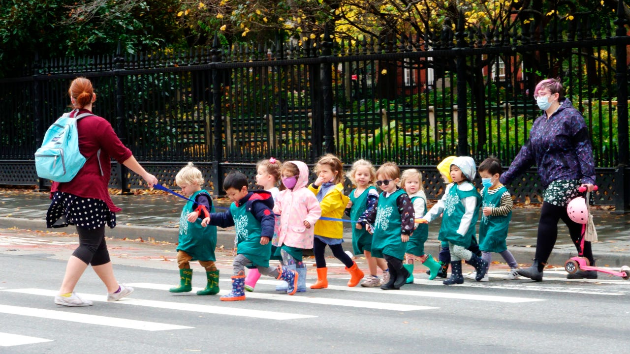 Line of pre-school children crossing street with teacher.