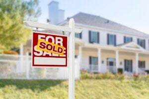 red and yellow "sold" sign in front of white suburban house with black shutters