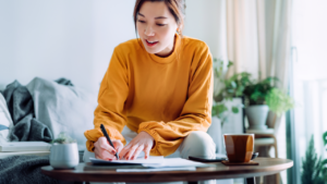 Young Asian woman holding a pen and signing paperwork in the living room at home. Deal concept