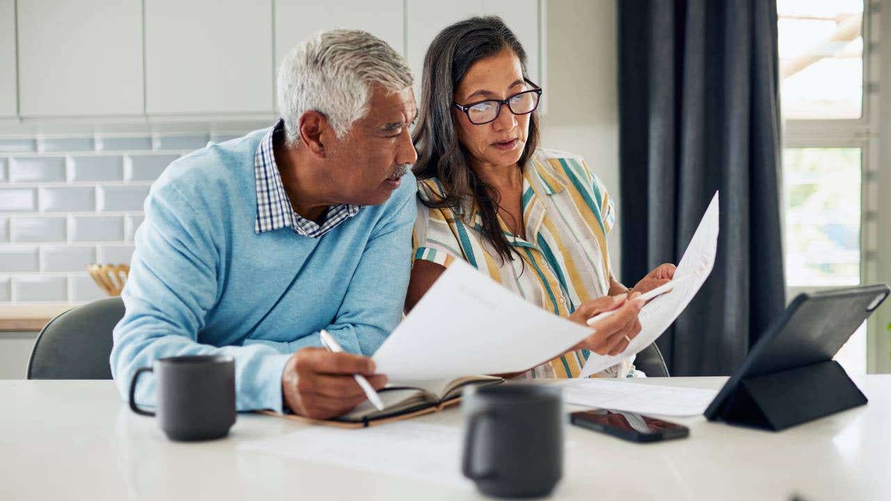 An older couple sitting in their kitchen reviewing their financial documents.