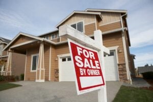 tan house with white trim and red "for sale by owner" sign out front