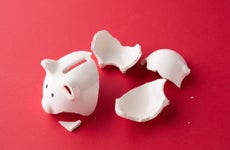 Broken whiter ceramic piggy bank in pieces on red surface