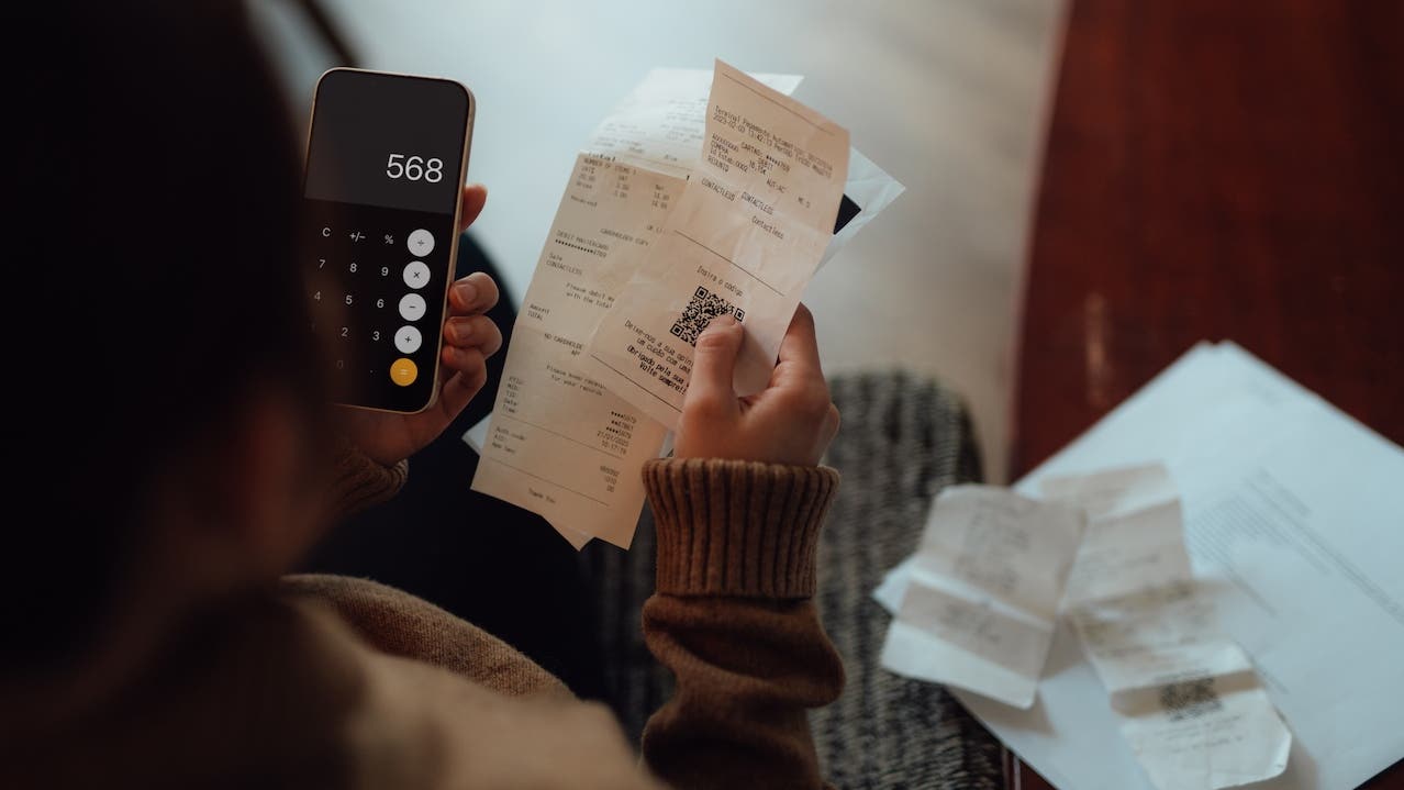 Over the shoulder view of young woman calculating bills and creating financial budget at home. Inflation and cost of living payment. Personal financial stress and wellbeing.