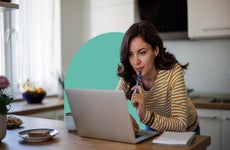 Woman sitting at table looking at open laptop with a blue half circle behind her