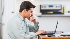 Married man sitting at kitchen table looking at laptop