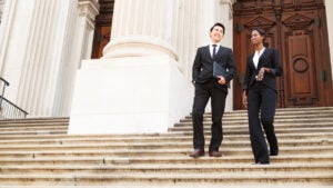 Two lawyers walk down the steps of a courthouse smiling to each other.