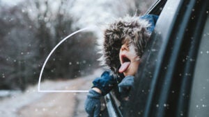 A child catching snowflakes from inside of a car