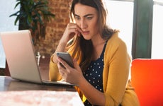 White woman looking at phone with open laptop beside her