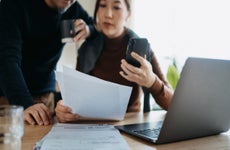 Asian couple consulting paperwork while working on a laptop together