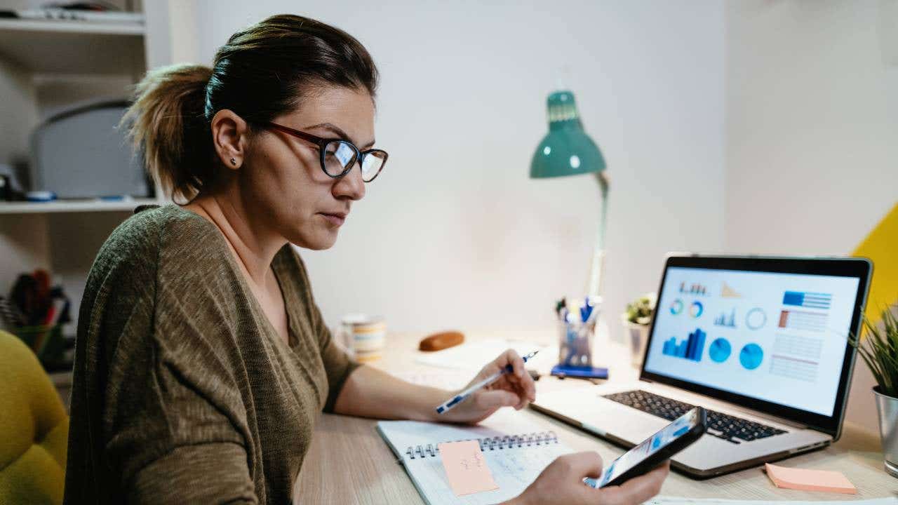 Person looking at pie charts and graphs on a laptop and their smartphone.