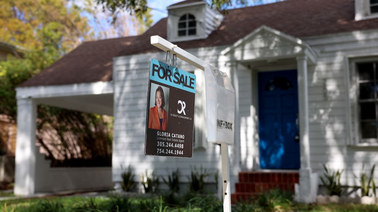 White suburban house with blue door and "for sale" sign out front