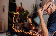 A man looks at a phone as he touches his forehead.