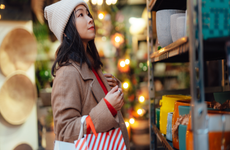 Young Asian woman with shopping bags choosing gifts at Christmas market