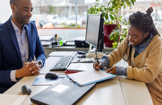 Female customer signing paperwork with car salesman sitting at office desk in dealership - stock photo