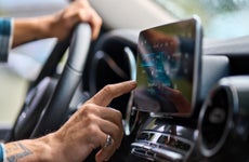 Close-up of a person's hand pressing a finger against a touchscreen on a car dashboard