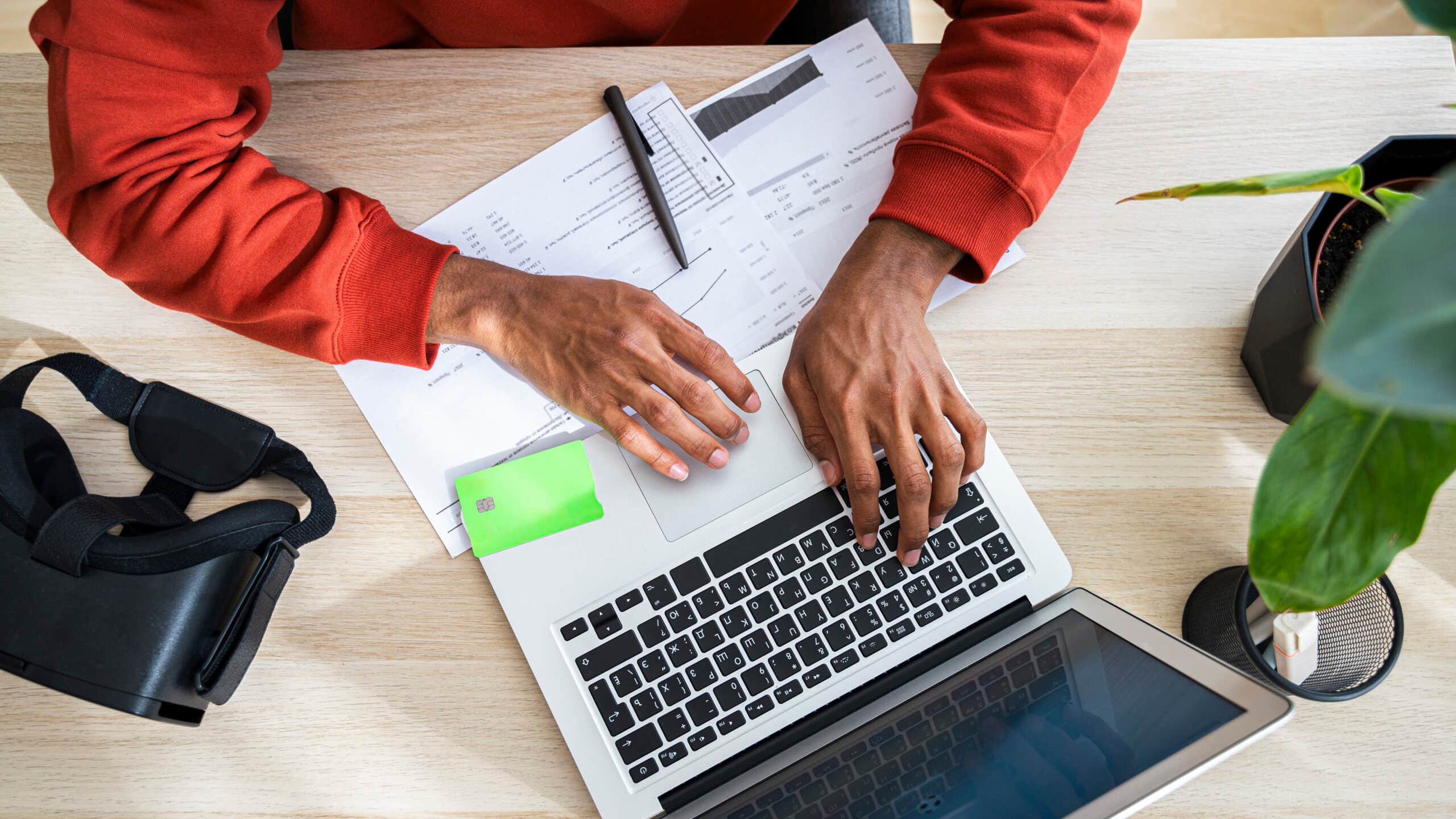 Freelancer working on laptop and reviewing documents at desk in home office