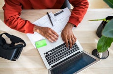 Freelancer working on laptop and reviewing documents at desk in home office