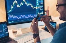 Trader holding a cold wallet in front of a monitor showing financial data