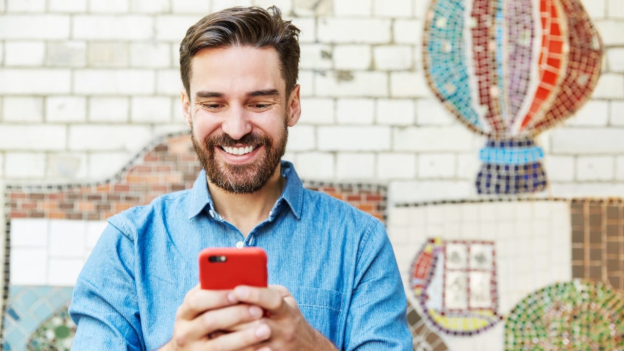 Man with smartphone next to tiled mosaic wall.