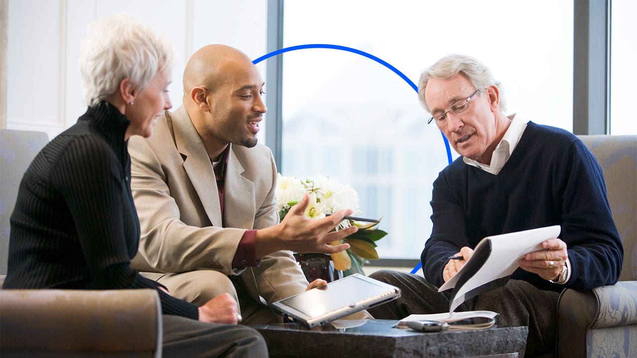 Business people review documents in front of a large window.