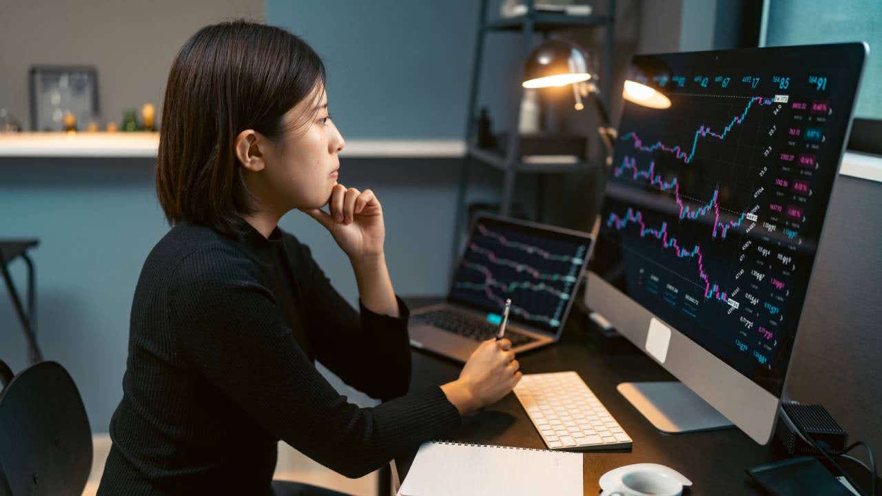 A young woman trades cryptocurrency on her computer at home at night.