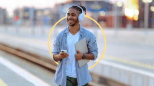 Man smiling with headphones on, phone in one hand and laptop in the other.