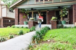 realtor putting for sale sign in front of brick house with big front porch