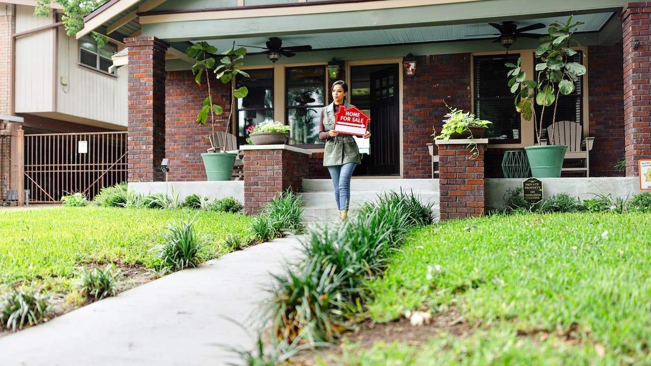 realtor putting for sale sign in front of brick house with big front porch