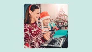 A woman and child in holiday attire look at a computer while holding a credit card.