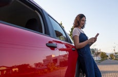 Woman looking at her mobile phone while leaning on a red car