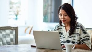 A woman uses her laptop while sitting at a table in her home.