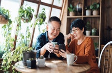 A happy senior couple video chats on their iPhone with coffee mugs in hand.