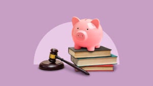 piggy bank standing on top of books with a gavel lying by the books