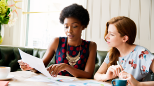 Two women with paperwork at table. - stock photo