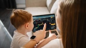 A woman checks her crypto trading account and points at the screen to show her toddler the graph.