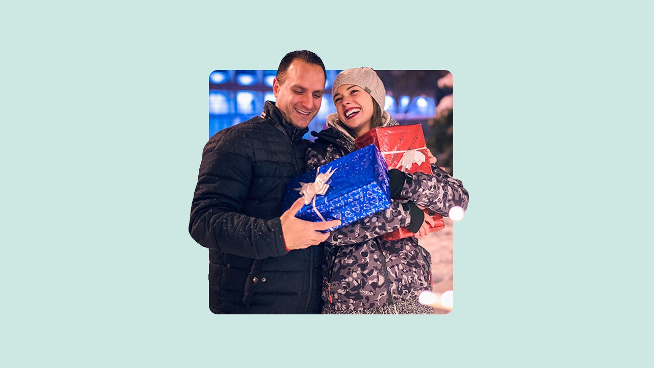 A smiling couple standing outdoors holding Christmas packages.