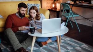 A young couple looks through documents while seated at a laptop computer.