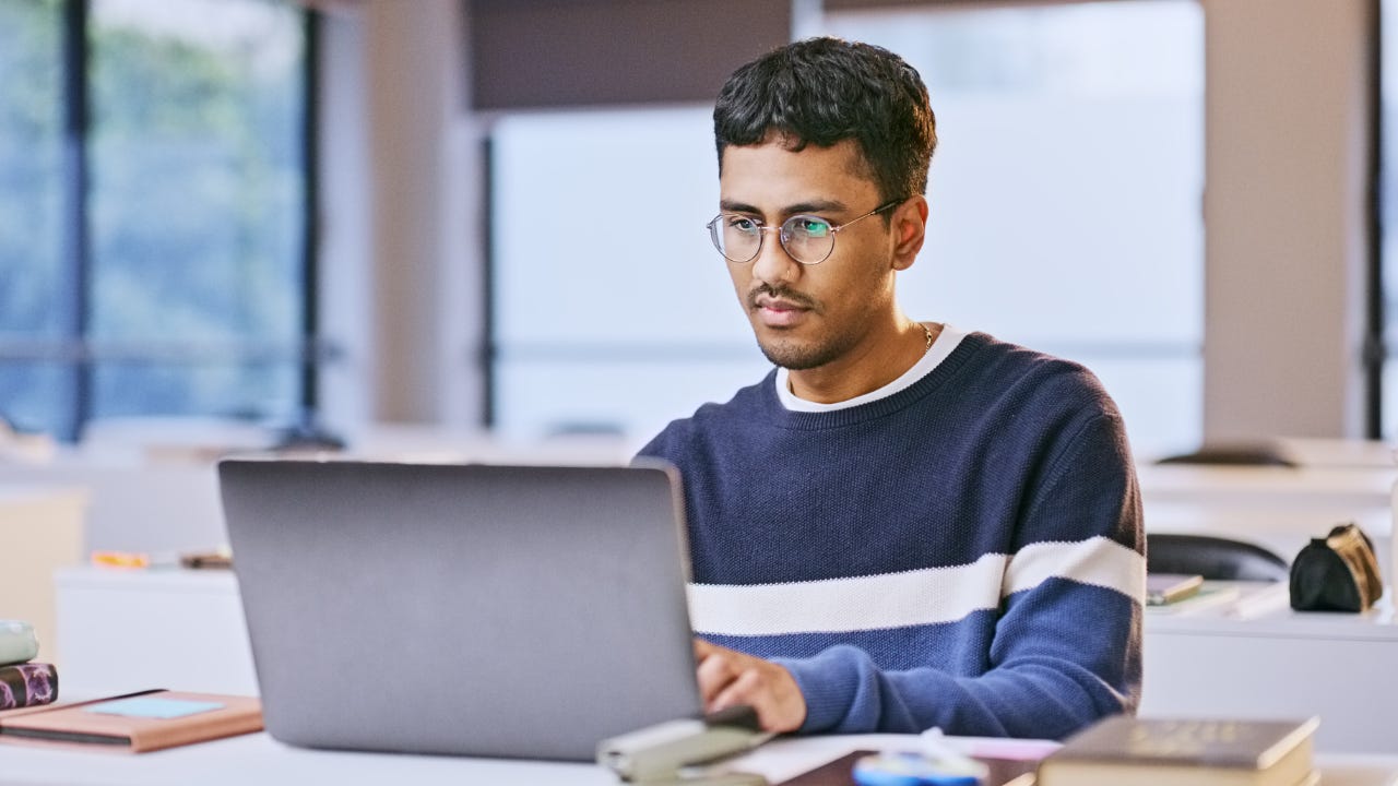 College student with glasses sitting at desk on laptop