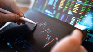 A hand holding a stylus up to a tablet displaying a stock chart.