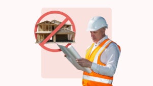 construction worker reading blueprints with red slash through large home under construction