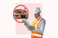 construction worker reading blueprints with red slash through large home under construction