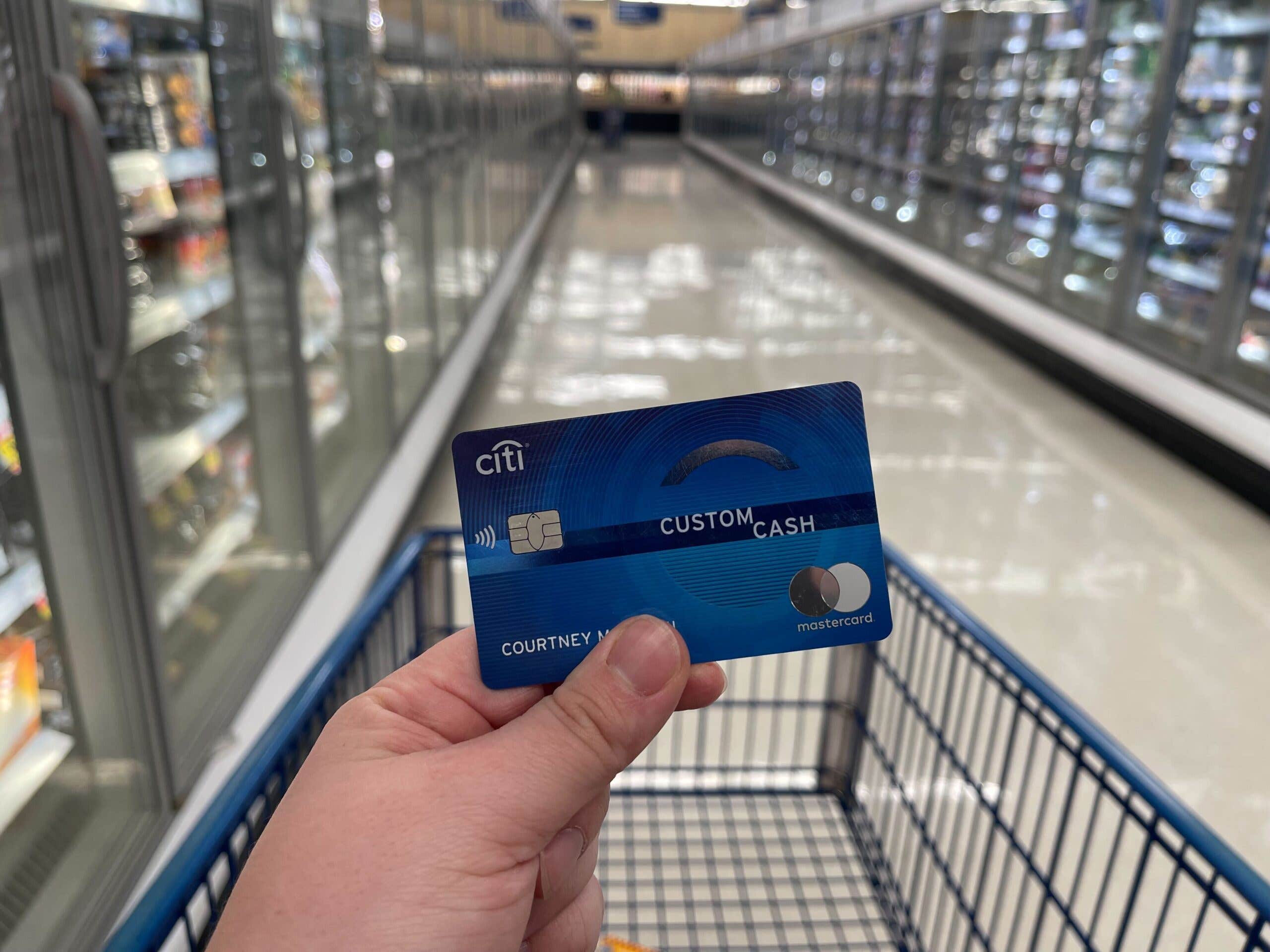 Closeup of a person holding a credit card over a grocery cart in a frozen food aisle.