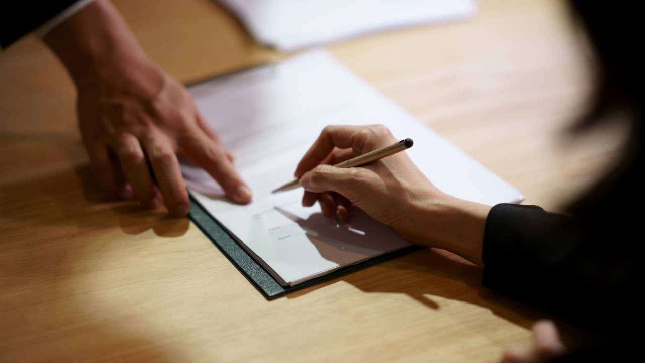 A close up of a man's hand pointing to where a woman should sign on a contract.