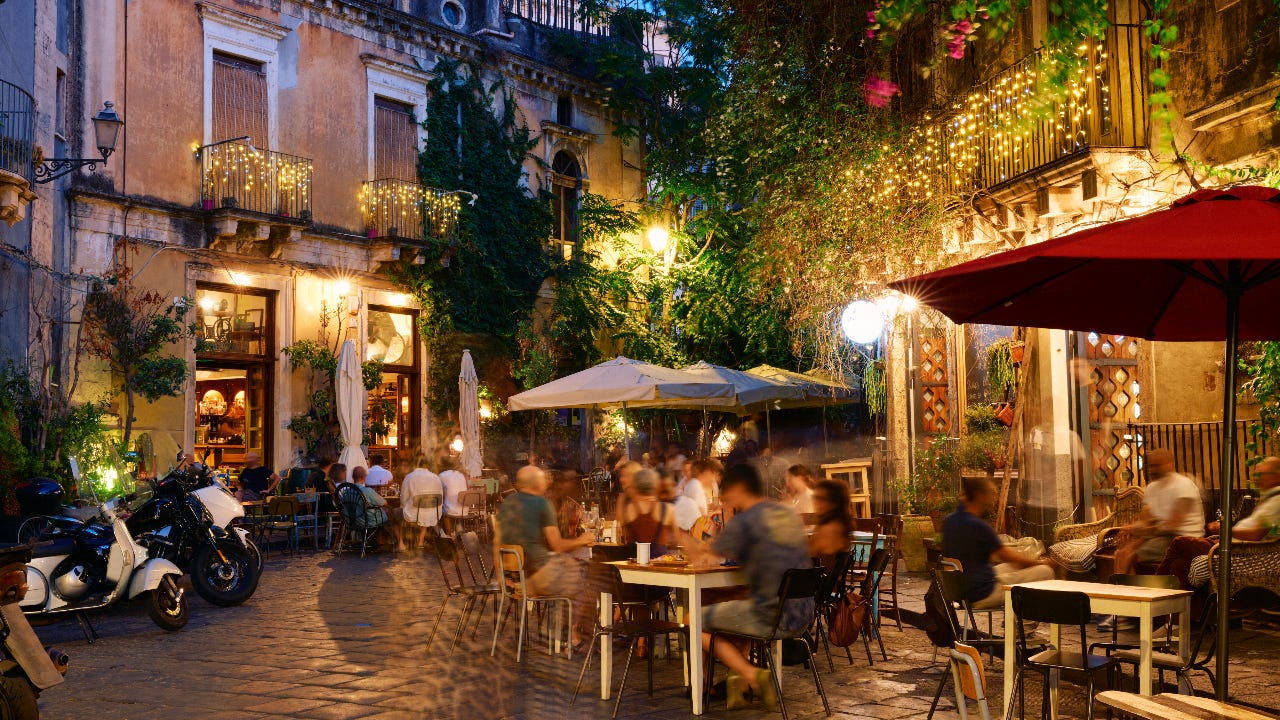 People dining outside restaurants and bars at dusk in Catania, Italy