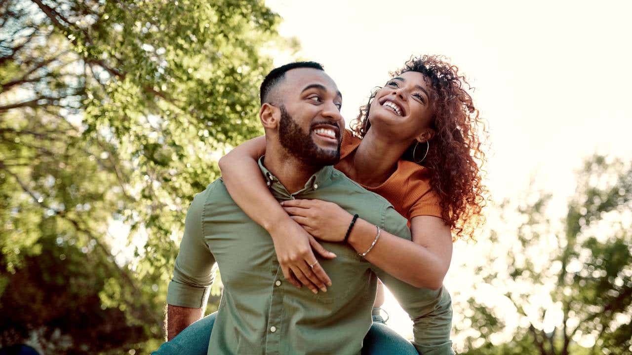 A young man giving his girlfriend a piggyback ride outdoors.