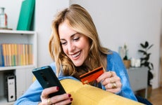 woman smiling holding her phone and a credit card