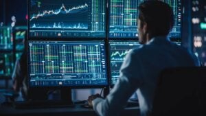 Person looking at four monitors displaying stock charts and data.