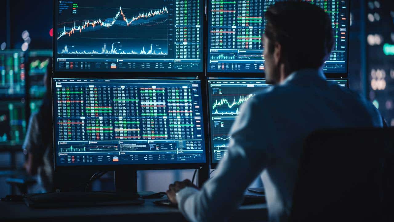 Person looking at four monitors displaying stock charts and data.