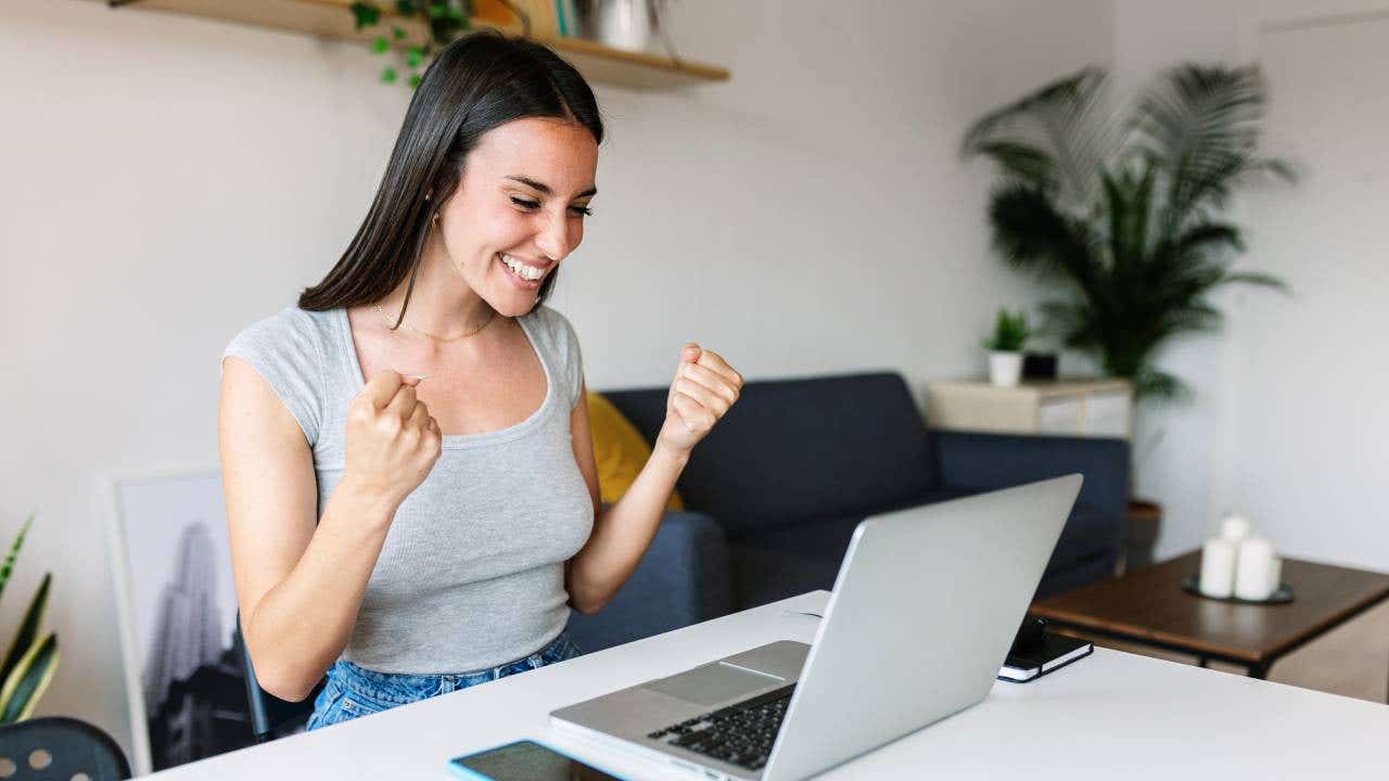 A woman celebrates while looking at her laptop screen