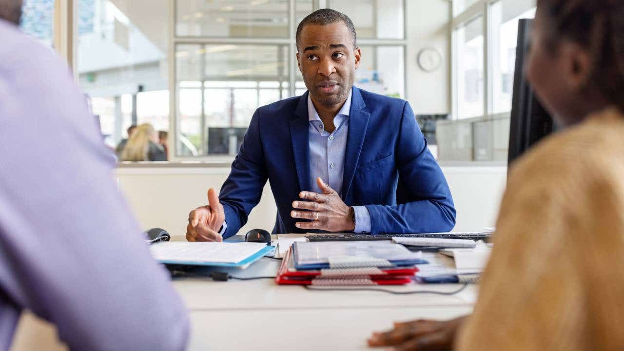 A man in a suit meets with a couple in his office.